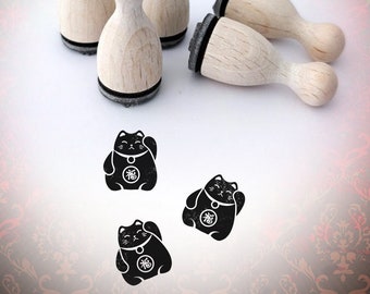 May include: Wooden stamps with black ink pads and a Maneki-neko cat design. The stamps have a light wood finish and are arranged with three upright and two lying down. Three black cat stamps are also visible.