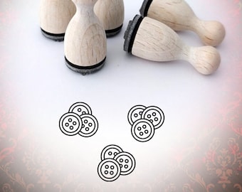 May include: Five wooden stamps with black ink pads, shaped like a rounded rectangle, arranged on a white surface. The stamps are designed to create images of buttons.