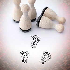 May include: Wooden stamps with a rounded handle and a black base are scattered across a patterned background. The stamps are accompanied by three ear-shaped graphic designs. The text "Bloody Nose" is visible in the upper right corner.
