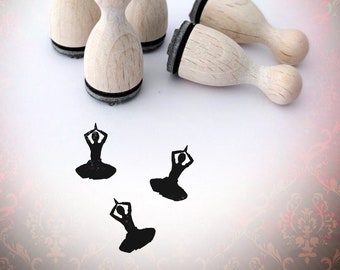 May include: Four wooden stamps with black ink pads, each featuring a silhouette of a person in a yoga pose. The stamps are arranged on a white surface with three additional impressions of the yoga pose stamp.