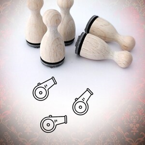 Könnte beinhalten: Vier Holzstempel mit schwarzen Stempelflächen, geformt wie eine Bowlingkugel, mit einem Design eines Pfeifens auf der Oberseite. Die Stempel befinden sich auf einer weißen Oberfläche mit einem roten und goldenen Muster im Hintergrund.