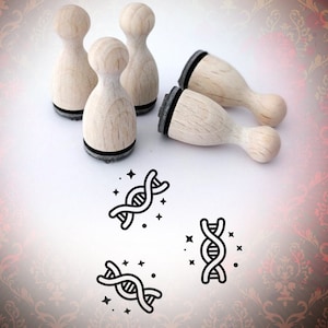 May include: Four wooden rubber stamps with black ink pads and a design of a DNA strand with stars. The stamps are on a white surface with a red and brown patterned background.