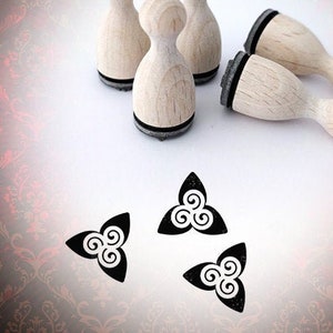 Könnte beinhalten: Vier Holzstempel mit schwarzen Stempelflächen und einem schwarz-weißen Design einer dreifachen Spirale. Drei weitere schwarz-weiße dreifache Spiralenstempel sind auf einer weißen Oberfläche zu sehen.