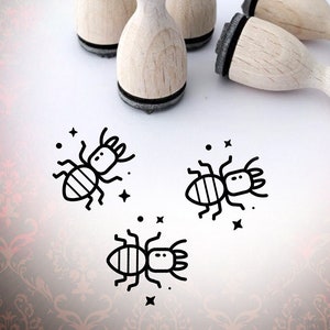 May include: Set of five wooden stamps featuring a simple line drawing of an ant. The stamps are round and have a black base. The stamps are arranged on a white surface with three of the stamps in a row and two stamps on either side of the row.