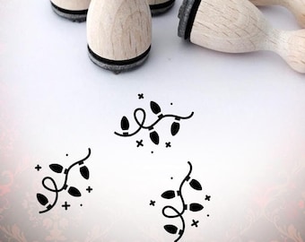 May include: Four wooden stamps with black ink pads, each featuring a design of a string of Christmas lights with stars. The stamps are arranged on a white surface. The text "Bloody Nose" is visible in the background.