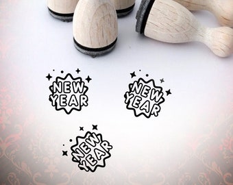 May include: Four wooden stamps with black ink pads, each featuring a black and white illustration of the words "New Year" in a speech bubble with stars.