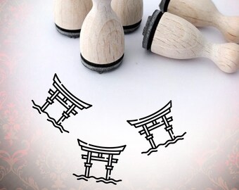 May include: Four wooden stamps with black ink pads, each featuring a simple line drawing of a Japanese torii gate. The stamps are arranged on a white surface with three torii gate stamps printed nearby.