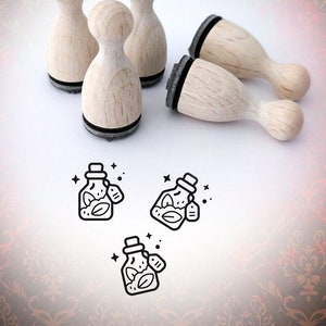 Könnte beinhalten: Satz mit fünf Holz-Stempeln mit schwarzem Stempelkissen. Jeder Stempel zeigt eine Strichzeichnung einer Flasche mit einem Blatt und einem Etikett. Die Stempel sind auf einer weißen Oberfläche mit einem roten und goldenen Muster im Hintergrund angeordnet.