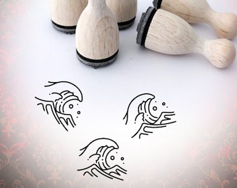 May include: Set of four wooden rubber stamps with black ink pads. The stamps feature a simple line drawing of a wave with bubbles. The stamps are arranged on a white surface with a red and gold patterned background.