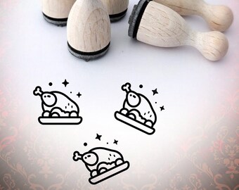 以下が含まれることがあります： 黒いインクパッドが付いた木製のゴム製スタンプ4個セット。各スタンプには、皿に載せられたローストチキンと周りに星が描かれた線画が描かれています。スタンプは白い表面に配置されています。