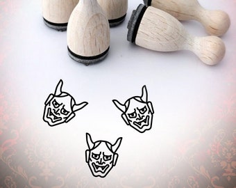 May include: Set of five wooden rubber stamps with black ink pads. Each stamp features a black and white illustration of a Japanese demon mask with horns. The stamps are arranged on a white surface.