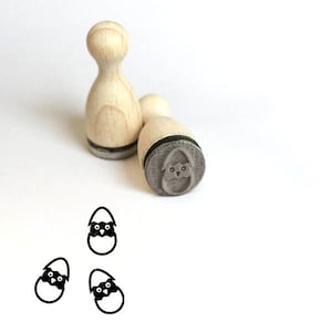 May include: Three wooden stamps with a black and white illustration of a chick hatching from an egg. The stamps are used to create a repeating pattern of the chick hatching from an egg.