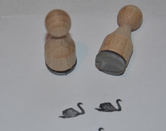 May include: Two wooden stamps with black rubber insets, each depicting a swan. The stamps are on a white surface, and there are three swan impressions made with the stamps.