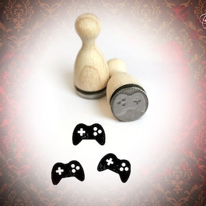 May include: Three wooden stamps with black ink pads. Each stamp features a black and white illustration of a video game controller.