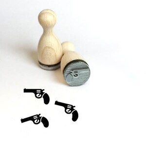 Könnte beinhalten: Zwei Holz-Stempel mit Pistolenmotiv. Die Stempel sind nicht eingefärbt und einsatzbereit.