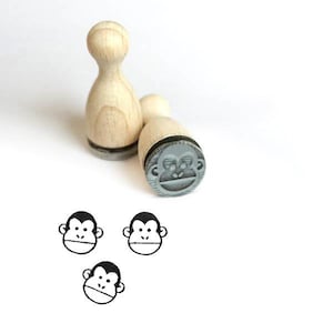 Könnte beinhalten: Drei Stempel aus Holz mit Affengesichtern. Die Stempel sind rund und haben ein graues Affengesicht mit schwarzen Augen und einem Mund. Die Stempel befinden sich auf einem weißen Hintergrund.