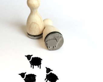 May include: Two wooden stamps with black sheep designs. The stamps are round and have a raised design. The sheep are facing to the right. There are three black sheep stamps printed on a white surface.