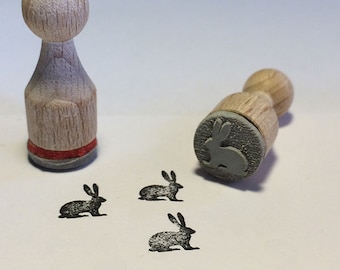 May include: Three small rubber stamps with a bunny rabbit design. The stamps are made of wood and have a gray rubber surface. The stamps are on a white surface.