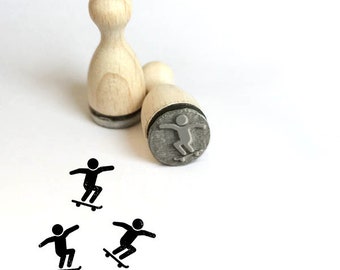 Op de afbeelding: Houten rubberen stempel met een skater ontwerp. De stempel heeft een houten handvat en een grijze rubberen stempel met een skater afbeelding. Drie zwarte skater afbeeldingen worden ook weergegeven op een witte achtergrond.