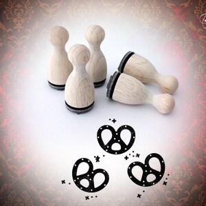 May include: Four wooden stamps with black ink pads, each featuring a different pretzel design. The stamps are arranged on a white surface with three pretzel designs stamped in black ink below them.