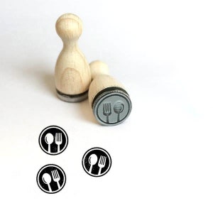 Peut inclure: Deux tampons en bois avec un tampon d'encre noir. Les tampons sont ronds et présentent un motif de fourchette et de cuillère. Les tampons sont sur un fond blanc.