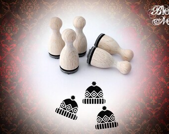 May include: Five wooden stamps shaped like a rounded rectangle with a black base. The stamps are arranged in a semi-circle. Three of the stamps are laying down and two are standing upright. The stamps have a design of a winter hat with a pom-pom on top. The hats have a geometric pattern.