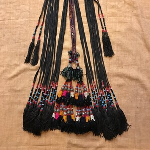 May include: A black beaded and tassel necklace with a central decorative piece. The necklace has a variety of colorful beads and tassels.