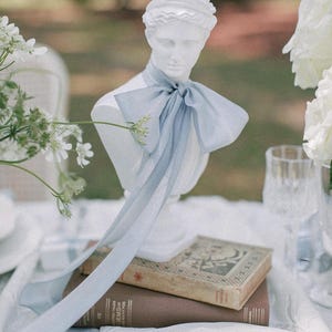 hand-dyed french blue silk ribbon tied on a white bust in a bow with long ends hanging down on a wedding reception table