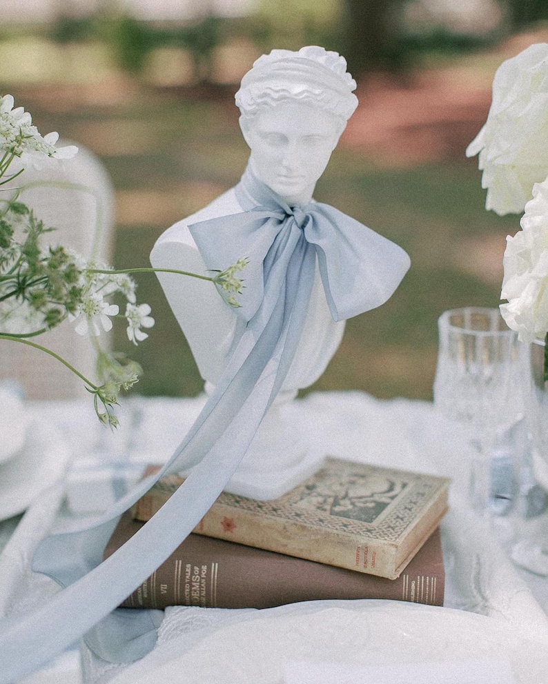 hand-dyed french blue silk ribbon tied on a white bust in a bow with long ends hanging down on a wedding reception table
