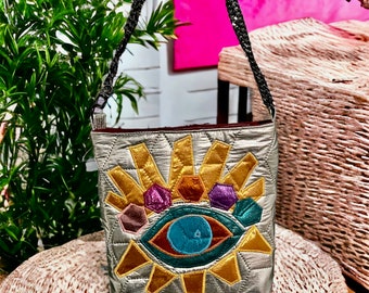 Metallic silver padded shoulder bag with an Eye Appliqué Detail, metal shoulder strap, medium size slouchy with a magnetic clasp for closure