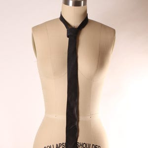 May include: A dark tie with a small dot pattern is displayed on a mannequin. The tie is knotted at the neck and hangs down, showing its length and texture. The mannequin is a neutral beige colour.