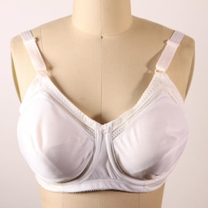 May include: A white bra with adjustable straps and a classic design. The bra features a full coverage style with a V-neckline and delicate lace detailing along the top edge. The bra is displayed on a mannequin.
