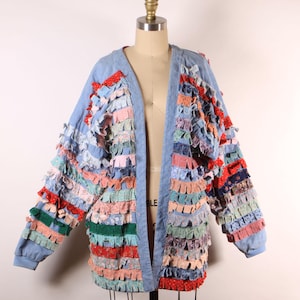 May include: A light blue denim jacket with a unique design featuring colorful fabric strips sewn around the edges, creating a layered and textured look.