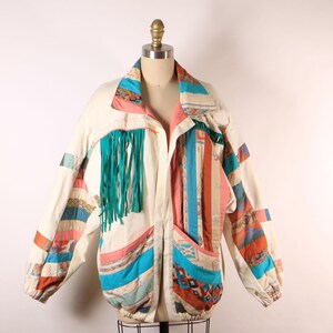 May include: A white jacket with a patchwork design featuring turquoise, pink, orange, and brown geometric patterns. The jacket has a zipper closure and a fringe detail on the front.