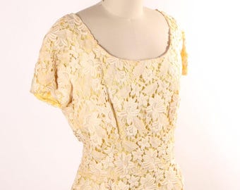 Puede incluir: Un vestido de encaje amarillo pálido con escote redondo y mangas cortas. El vestido está hecho de encaje floral delicado y tiene un corpiño ajustado y una falda completa.