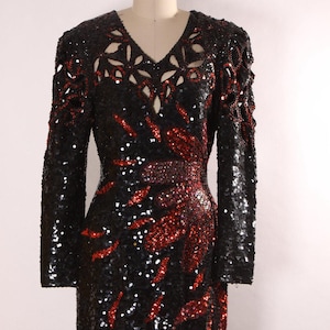 Puede incluir: Un vestido largo de lentejuelas negras con detalles de lentejuelas rojas. El vestido tiene un escote en V y un diseño de corte en el escote.