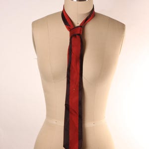 May include: A necktie featuring a vibrant red center panel flanked by two dark brown vertical stripes. The tie is tied in a simple knot and rests against a beige mannequin torso that has the text COLLAPSIBLE SHOULDER and the number 2 printed on it.