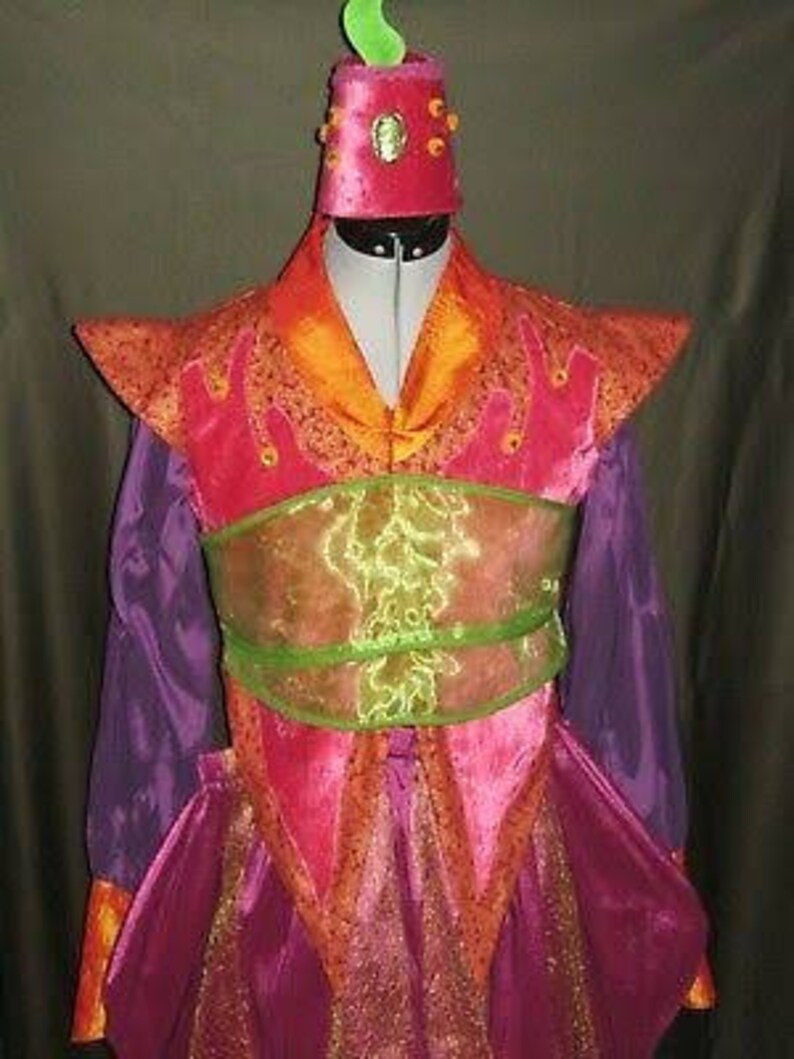 Puede incluir: Un disfraz vibrante con un corpi&ntilde;o rosa y naranja, mangas moradas y un sombrero a juego. El disfraz presenta una faja verde y dorada y adornos decorativos naranjas. El sombrero tiene un acento verde en forma de llama.