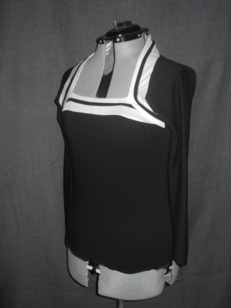 Puede incluir: Un top negro de manga larga con cuello cuadrado y ribete blanco. La parte superior se muestra en un maniqu&iacute;, mostrando su dise&ntilde;o y ajuste. La silueta elegante de la prenda y los colores contrastantes crean una est&eacute;tica moderna.