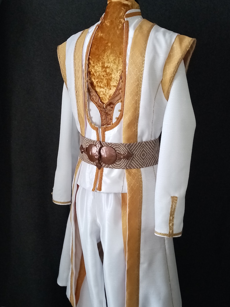 Puede incluir: Un disfraz blanco con detalles dorados, con cuello alto y mangas largas. El atuendo incluye un cintur&oacute;n decorativo y pantalones a juego. El disfraz es probablemente para una actuaci&oacute;n teatral o cosplay.