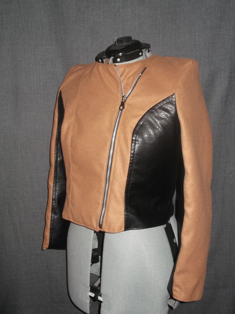 Puede incluir: Chaqueta marr&oacute;n y negra con cremallera diagonal. La chaqueta tiene un cuerpo marr&oacute;n con paneles negros de aspecto cuero en los laterales y las mangas. Se muestra en un maniqu&iacute;.