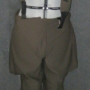 May include: A costume consisting of olive-green shorts and a matching bullet belt with gold-colored bullet casings. The outfit is displayed on a mannequin. The text "Little Monsters Couture" is visible at the bottom.