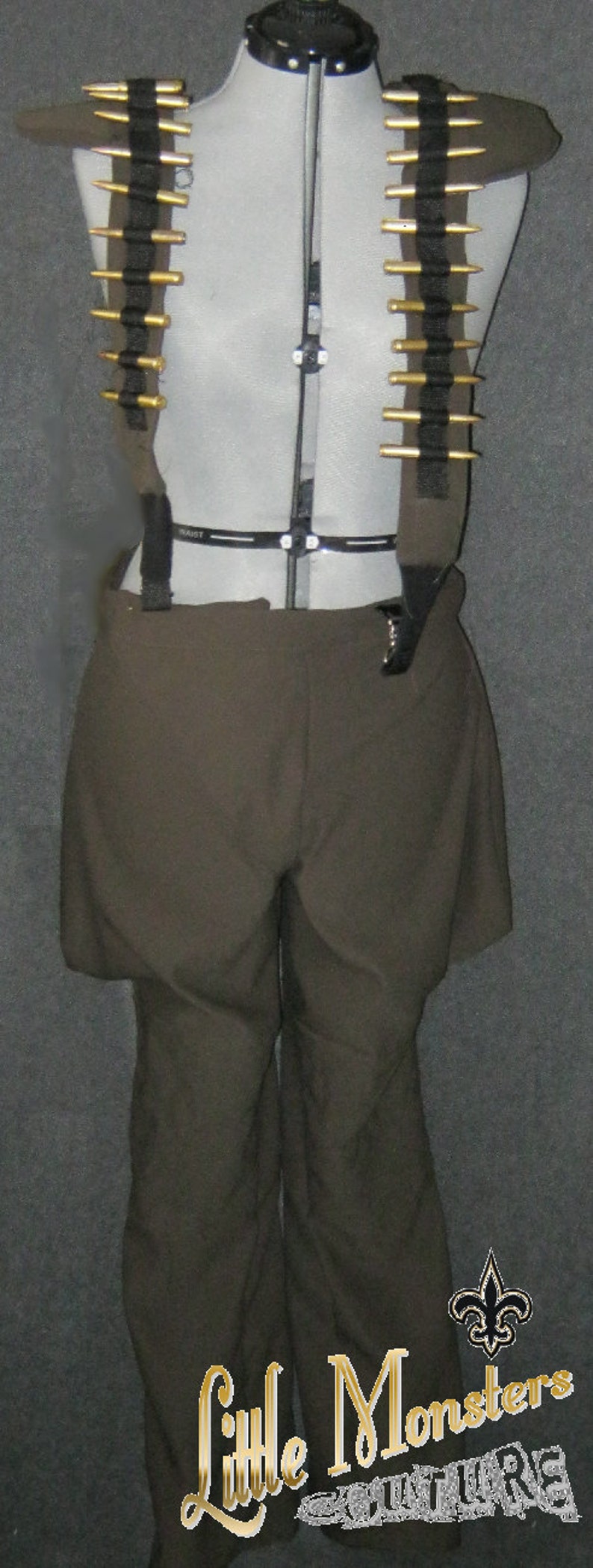 May include: A costume consisting of olive-green shorts and a matching bullet belt with gold-colored bullet casings. The outfit is displayed on a mannequin. The text "Little Monsters Couture" is visible at the bottom.