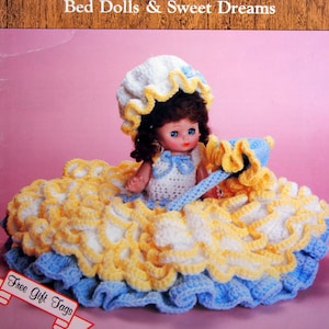 May include: A crochet doll pattern book titled "Claire Bed Dolls & Sweet Dreams" by Dumplin Designs. The cover features a crocheted doll wearing a white and yellow dress with a blue ruffle trim. The doll is holding a crocheted flower.