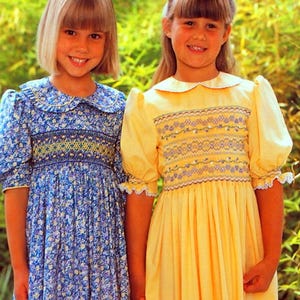 May include: Book cover titled "Smocking Inspiration" featuring two young girls in smocked dresses. One dress is blue with a floral pattern, the other is yellow. The cover has a blue floral border and text that reads "Margie Prestedge, Sheila Bennett."