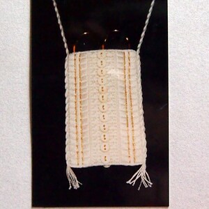 May include: A white needlepoint scissor case with gold thread accents and a dimensional stitch design. The case is hanging from a white cord and has a black background.