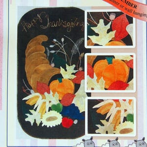 May include: A decorative Thanksgiving-themed wall hanging or table runner. The design features a cornucopia, pumpkins, and fall leaves. The text "Happy Thanksgiving" is visible. Finished size is 15" x 26".