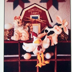 May include: A Homespun Farms design featuring a set of plush barn animals: a kitty, cow, and chicken. The scene includes a red barn, star-shaped decorations, and a wooden shelf with eggs. The text "Barn Babies" is at the top.