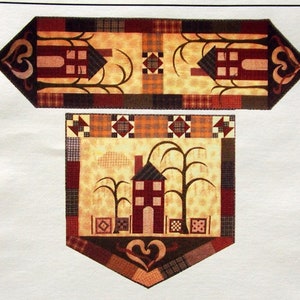 May include: A quilting pattern for a table runner and banner featuring a house with trees and a heart design. The pattern is titled "Our House" and is by Vicki Arnold & Pat Gates. The pattern is from Sew Many Visions.