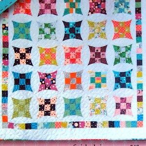 May include: A quilt pattern featuring a 1950's style design with a flare. The quilt is made up of colorful squares and is finished to a size of approximately 54 inches by 63 inches. The pattern is shown with a group of women wearing 1950's style clothing.